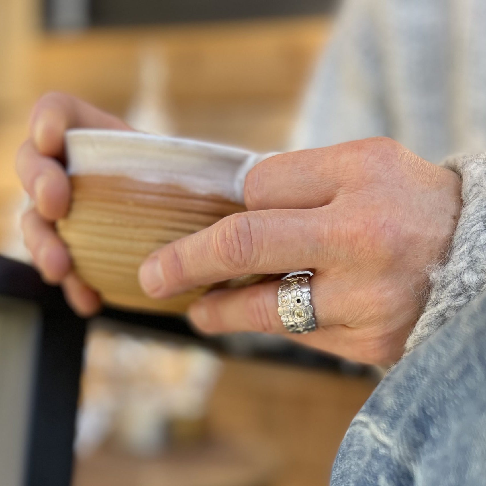 Person in a sweater sitting in an Adirondack chair drinking coffee with a beautiful silver colored ring on