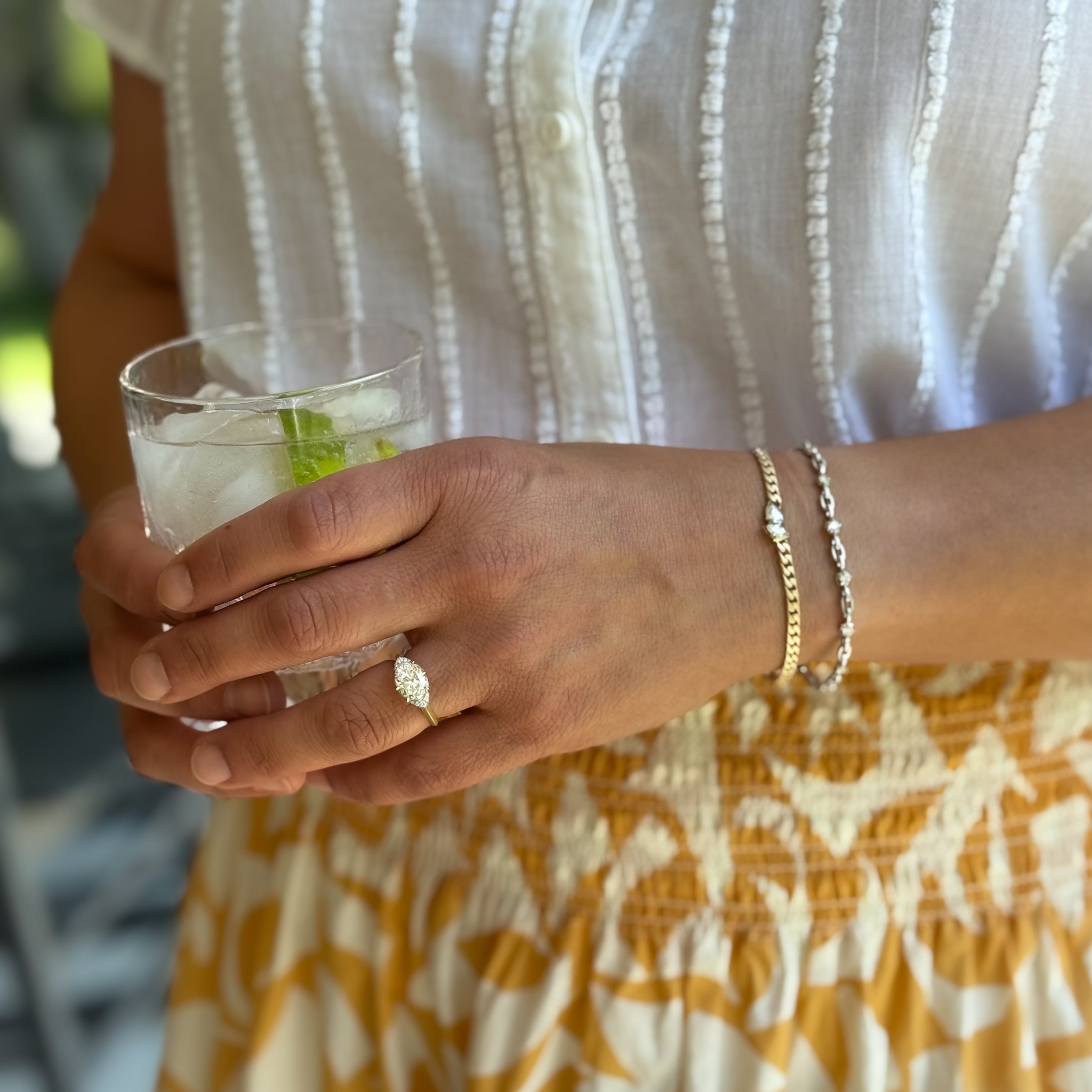 Woman in a yellow skirt and white top drinking with Jade Trau Ring and Bracelets on