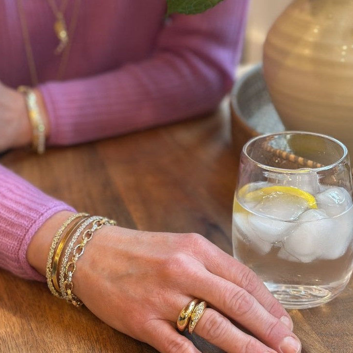 Woman in a white sweater over a blue dress wearing 3 gold and diamond bracelets