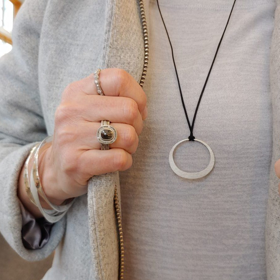 Man in grey wearing Toby Pomeroy Charm on a black cord necklace, two silver rings and bracelets