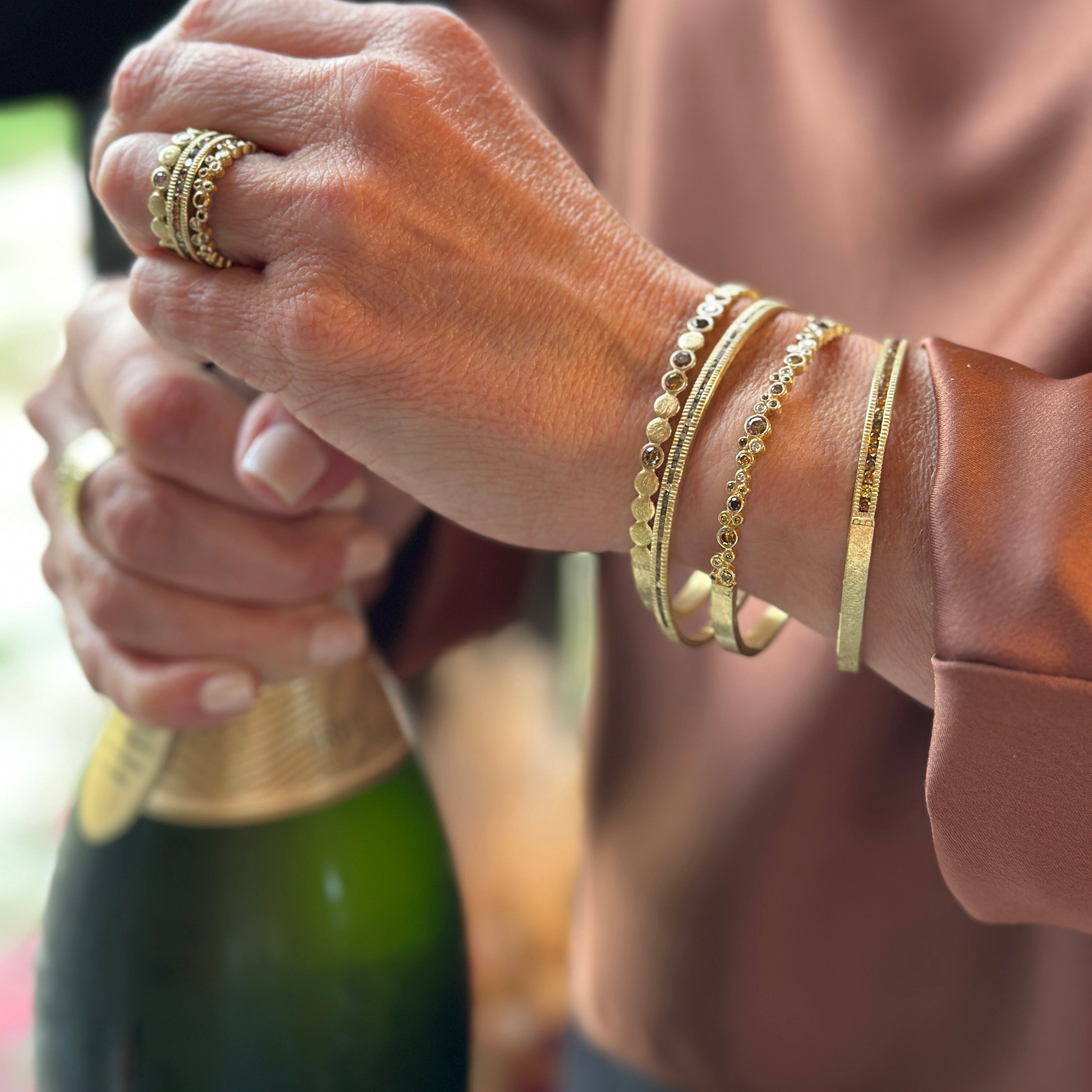 Woman opening a champagne bottle wearing 4 gold bracelets and a gold ring