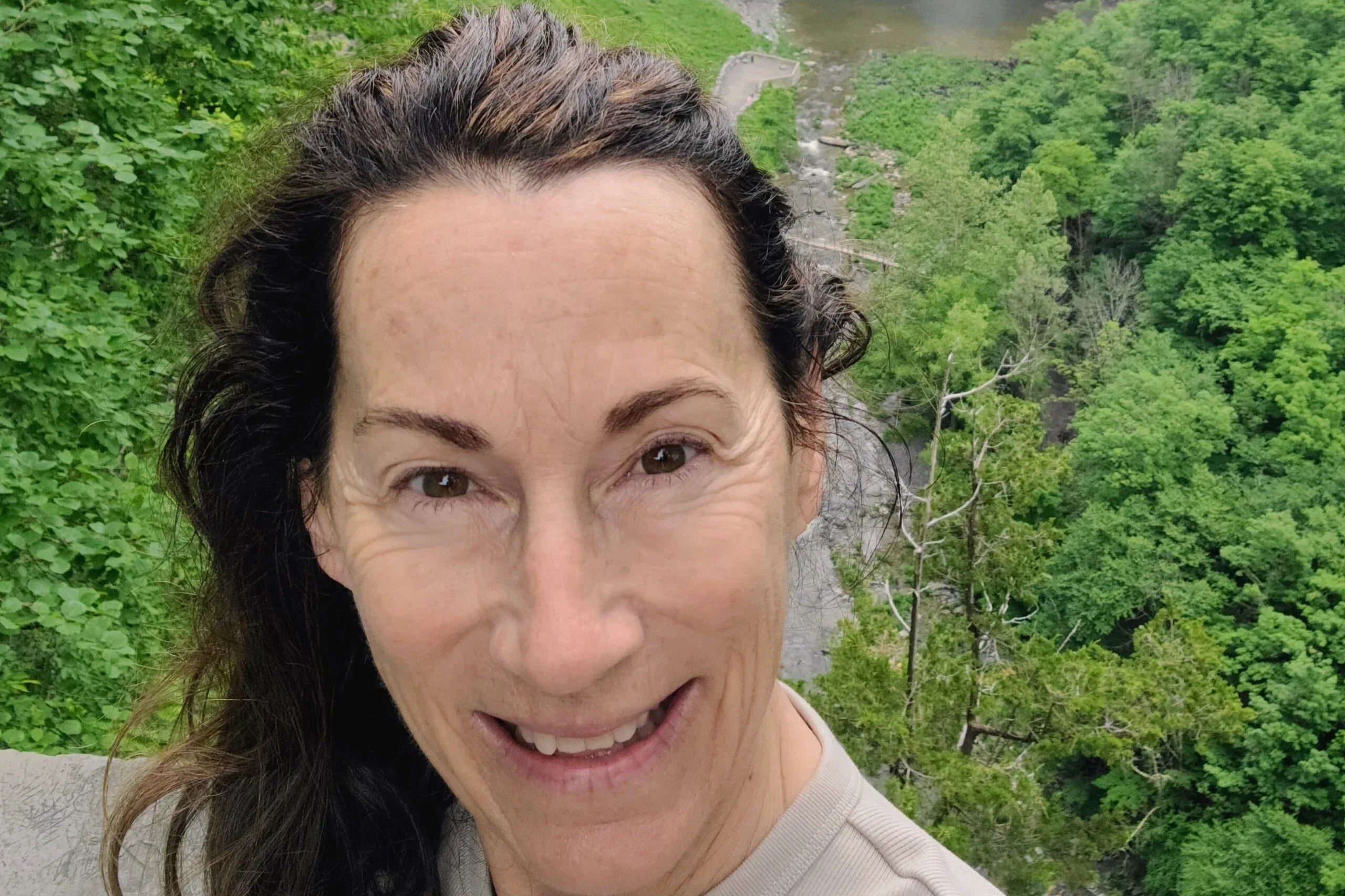 Woman taking a selfie with a scenic waterfall and lush greenery in the background. Carol Huber - Stratton Store Sales