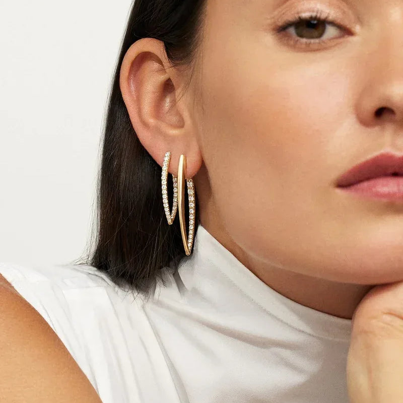 A woman in a sleeveless white top rests her chin on her hand, showcasing Yellow Gold and Diamond Hinged Hoop Earrings. Only the lower half of her face and ear are visible, drawing attention to the sparkling stones.