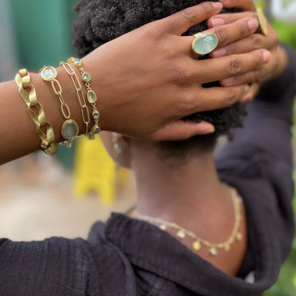 Person wearing gold bracelets and a ring with a blurred outdoor background