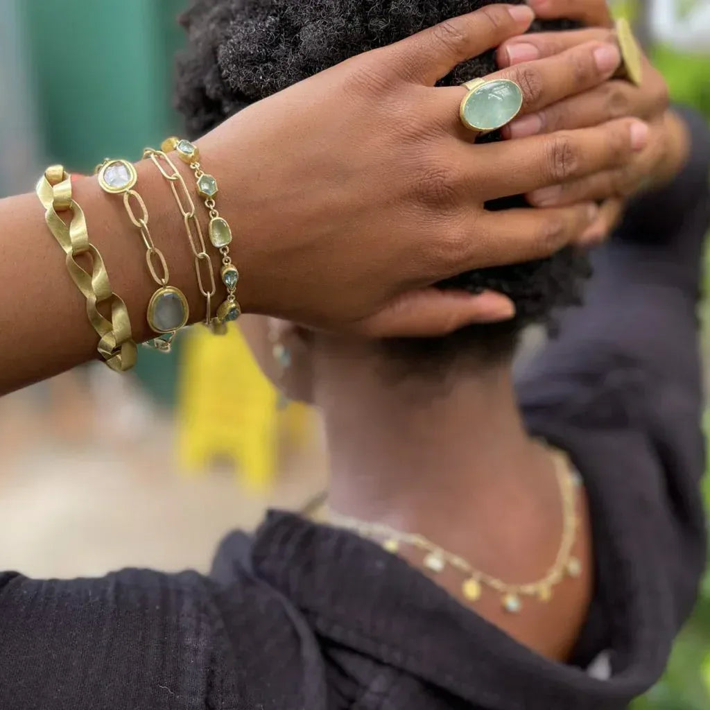 Person wearing gold bracelets and a ring with a blurred outdoor background