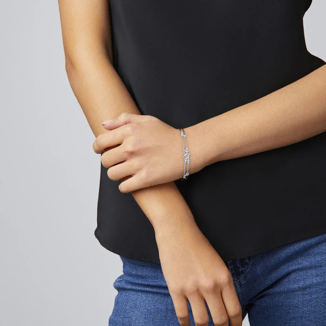 Person wearing a black top and blue jeans with gold bracelets on a gray background