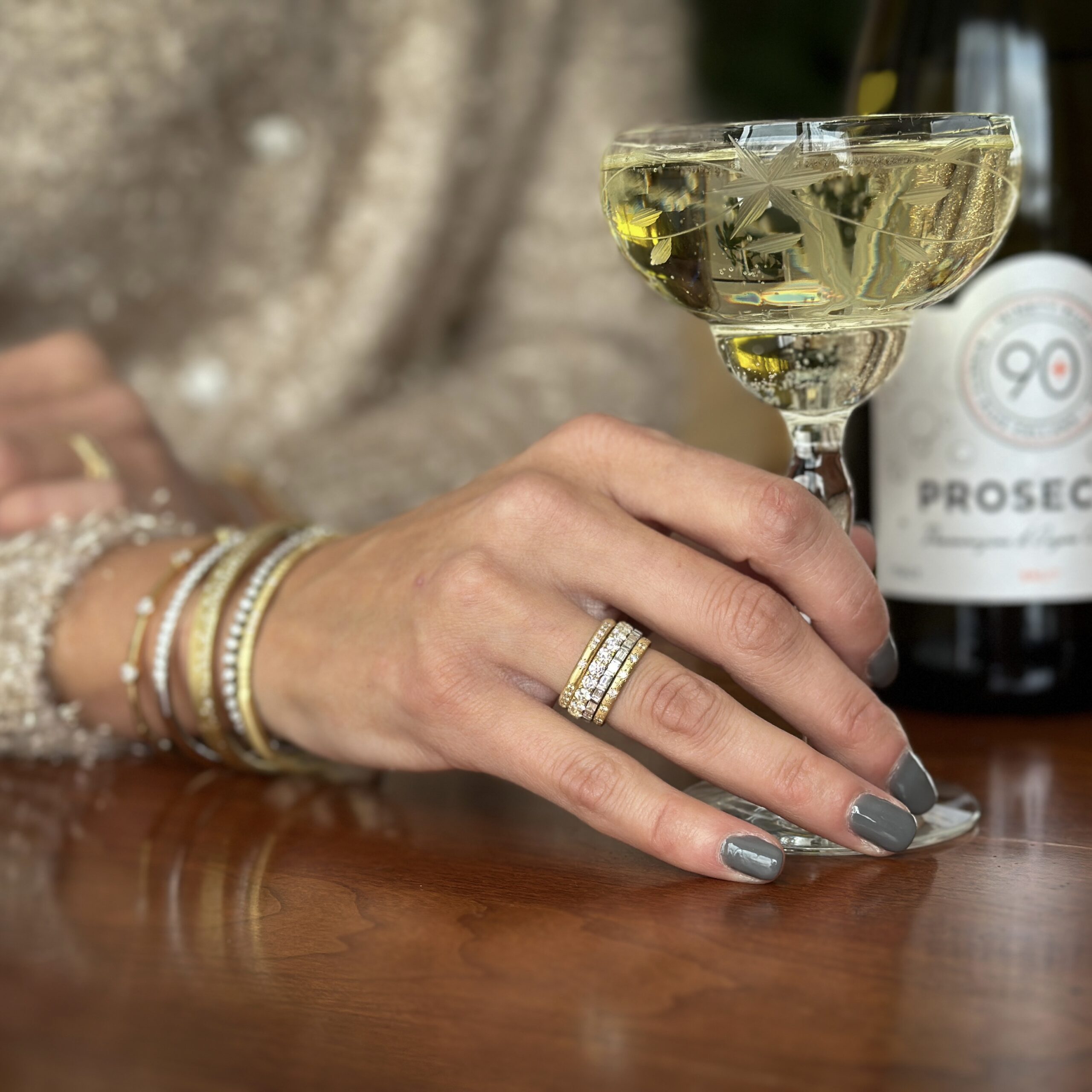 Woman holding a glass of prosecco wearing a ring and multiple bracelets
