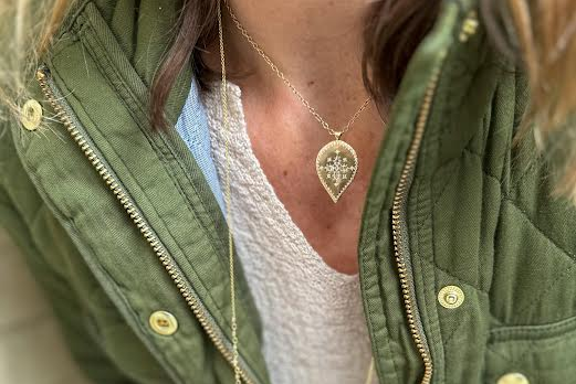 Woman in a green jacket and light top wearing a gold necklace and pendant