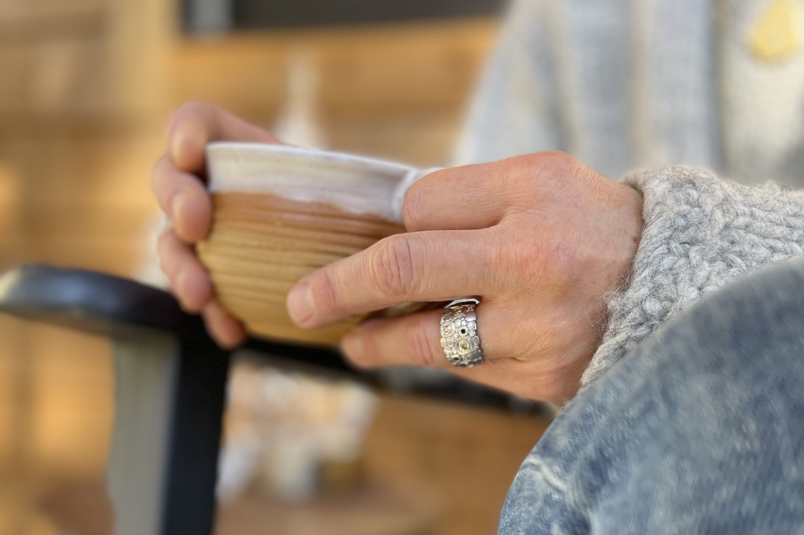 Person in a sweater sitting in an Adirondack chair drinking coffee with a beautiful silver colored ring on