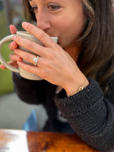 Woman drinking coffee in a black jacket wearing Mark Patterson ring and bracelet