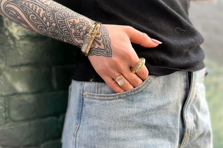 Tattooed woman leaning against a green wall wearing Moritz Glik bracelet and rings