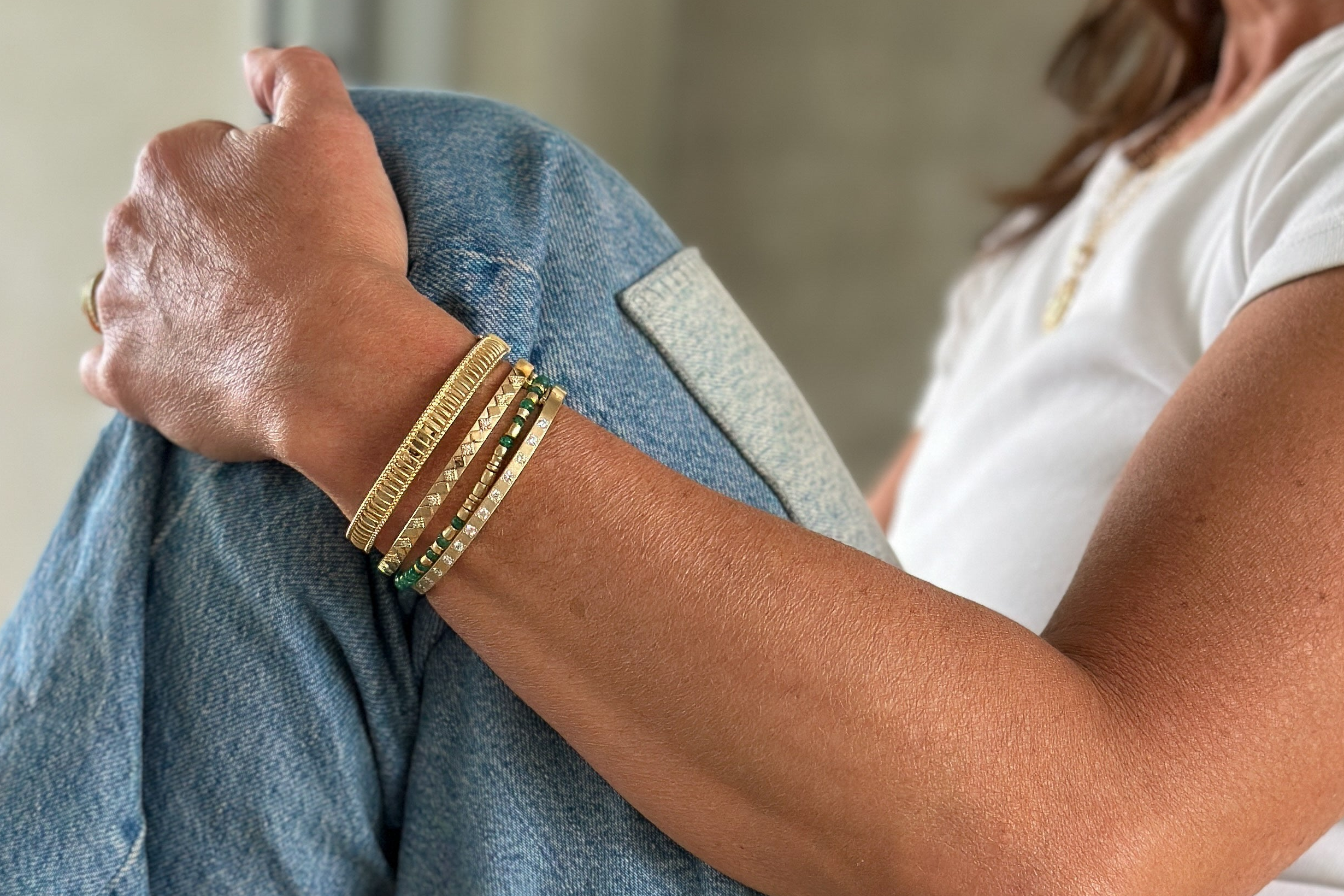 Woman in jeans sitting on the floor wearing gold Orly Marcel bracelets