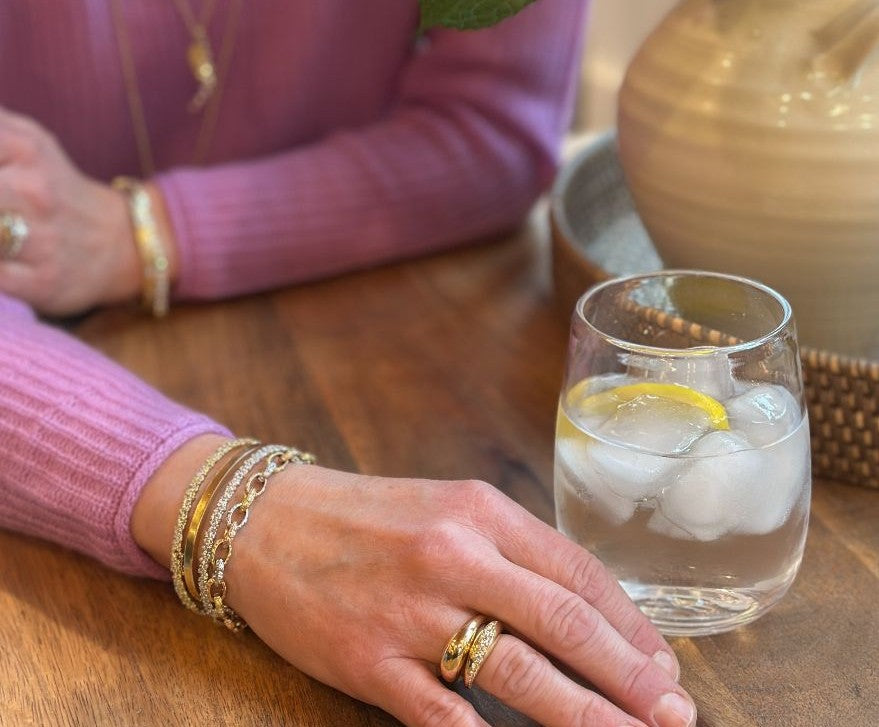 Woman in a white sweater over a blue dress wearing 3 gold and diamond bracelets