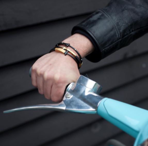 Person on a teal motor bike with a black jacket wearing 3 black and gold bracelets.