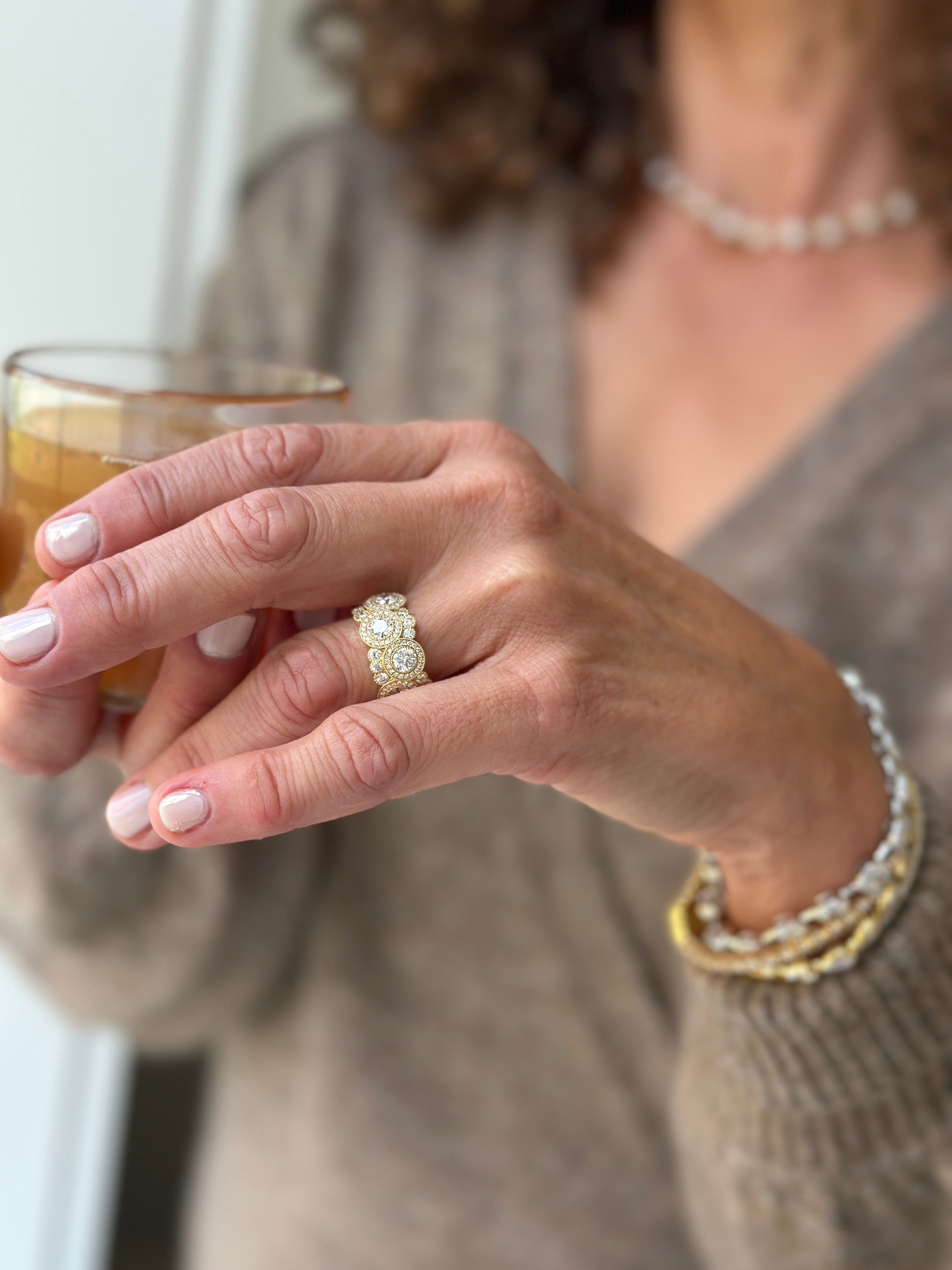 Woman holding a drink wearing Rahaminov gold and diamond ring and 3 gold bracelets