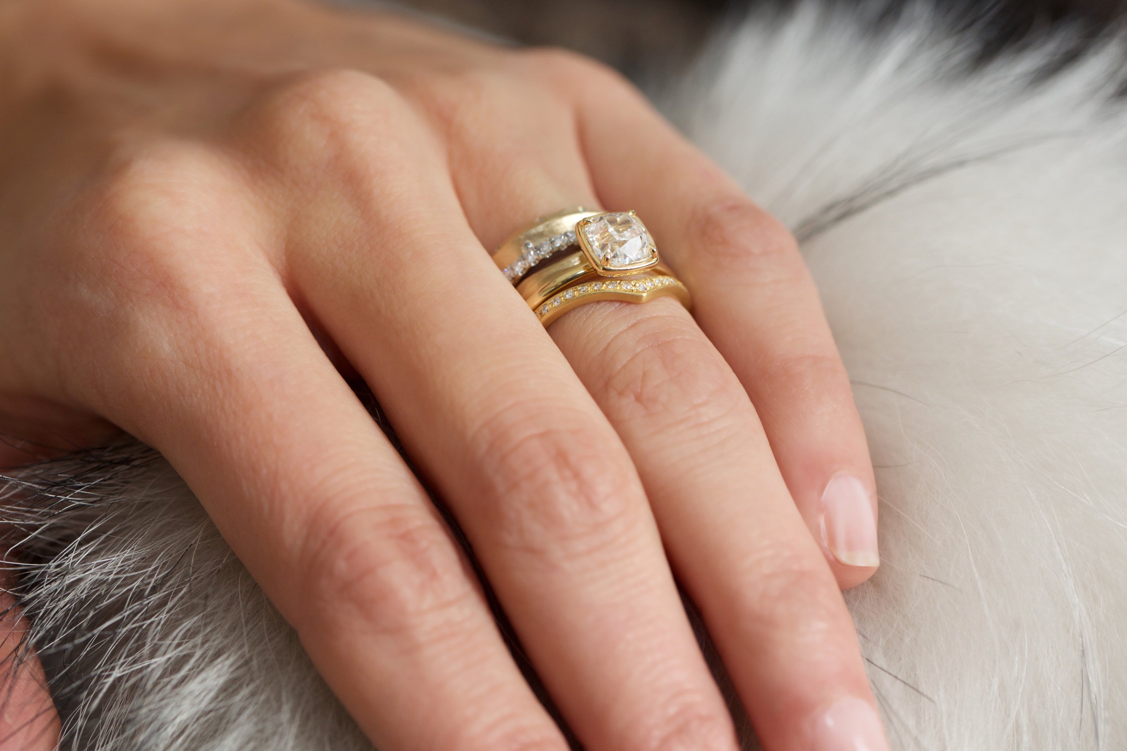 Woman's hand on top of white and grey fur wearing 3 gold, silver and diamond rings