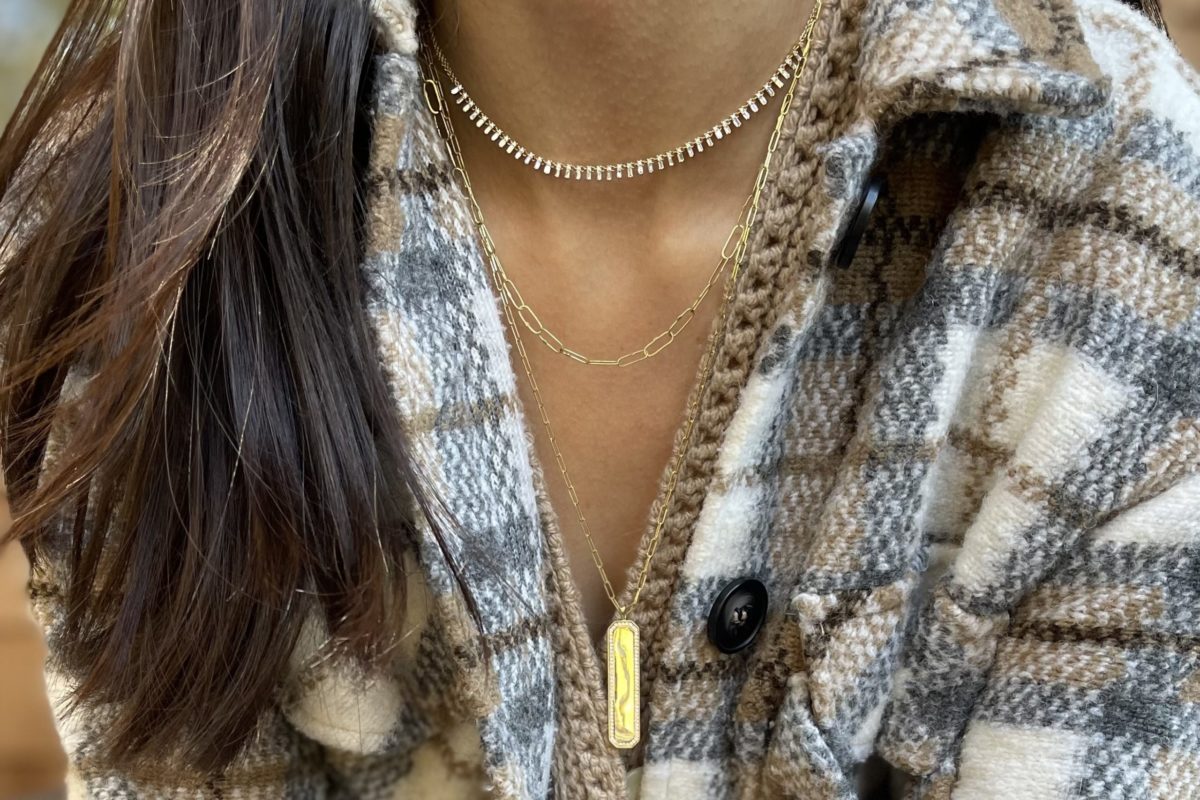 Woman with long dark hair wearing a light flannel and 3 gold chains, one with a long golden pendant
