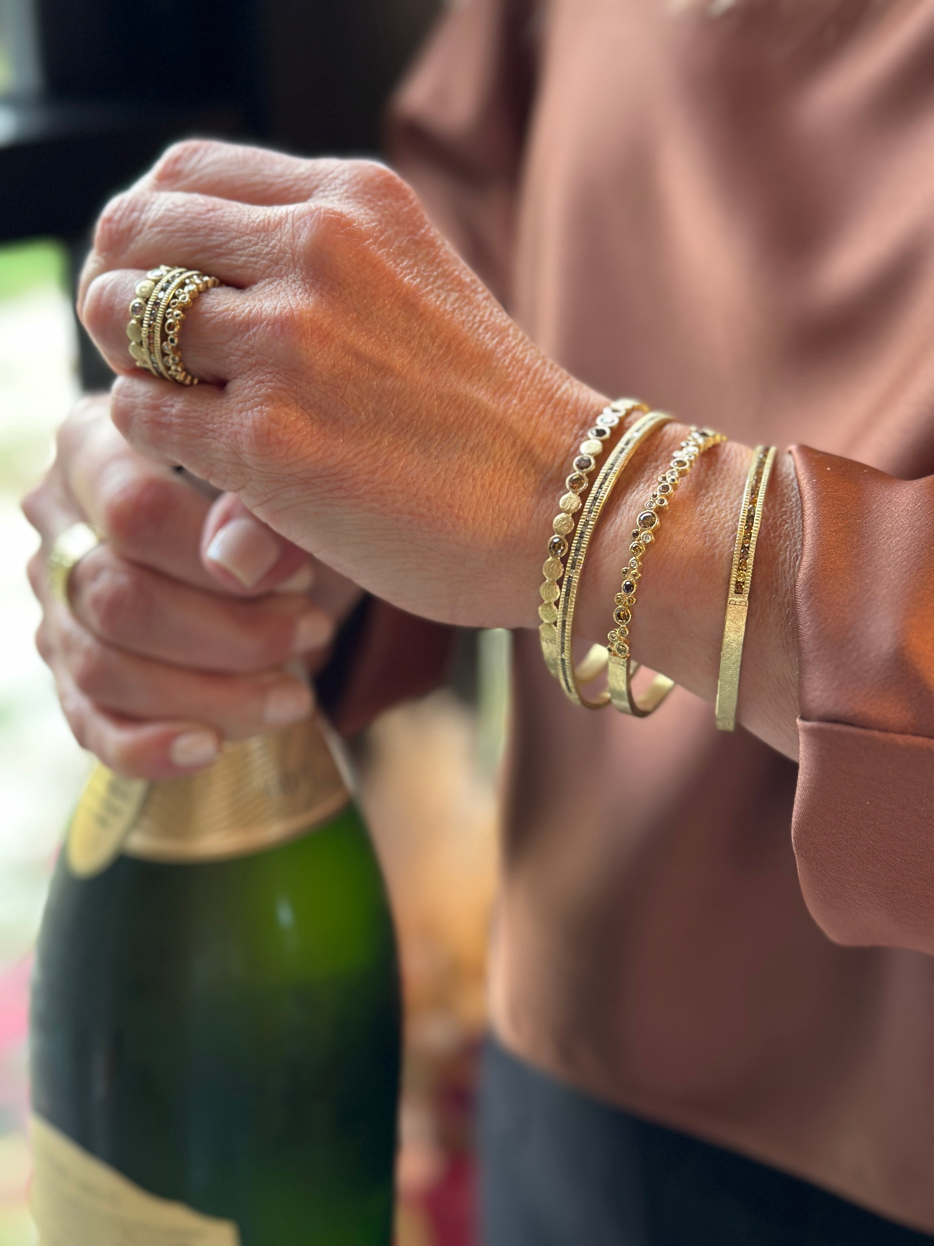 Woman opening a champagne bottle wearing 4 gold bracelets and a gold ring