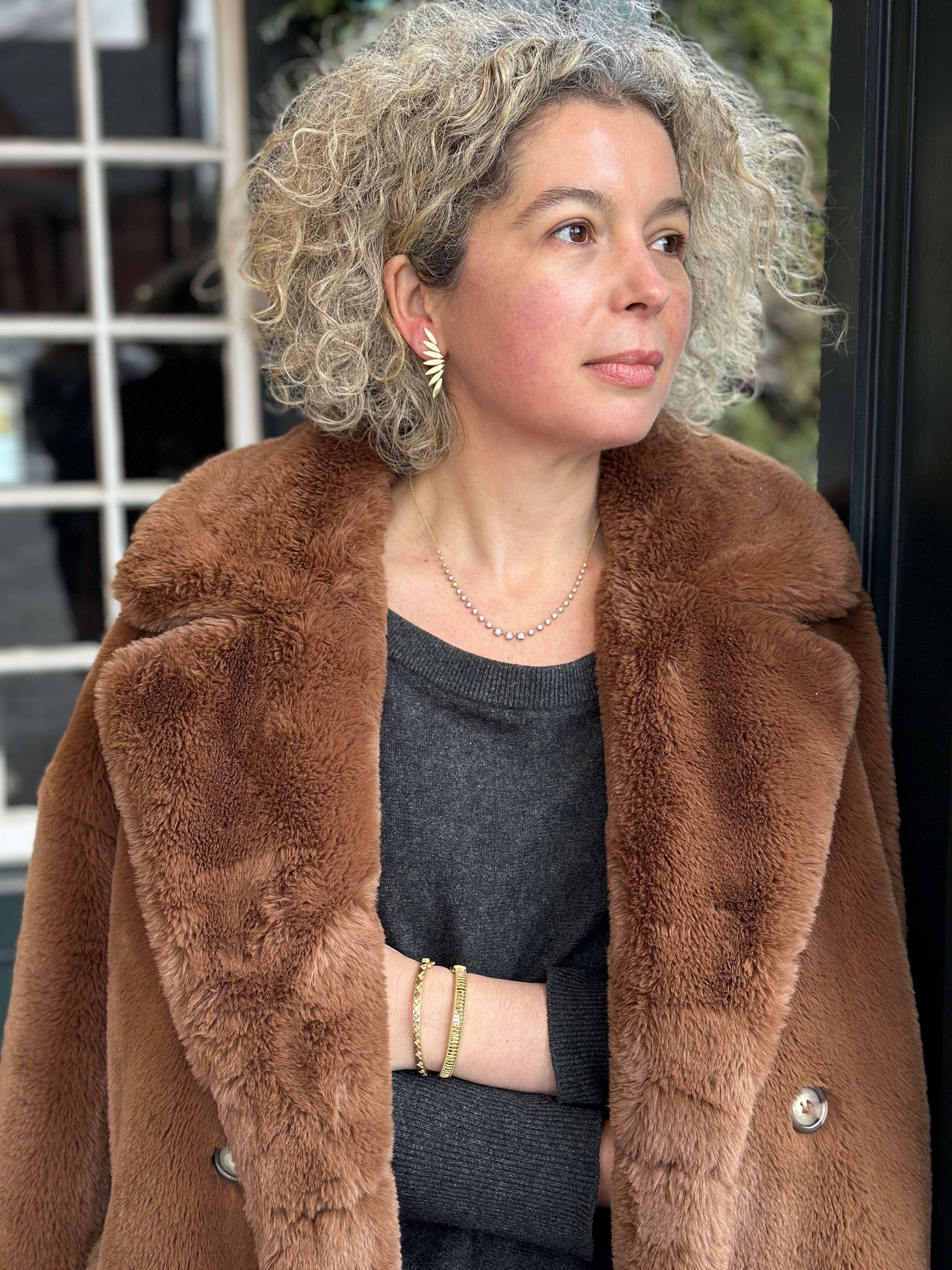 Woman wearing a brown fur coat and black top wearing Melissa Kay bracelets and earrings