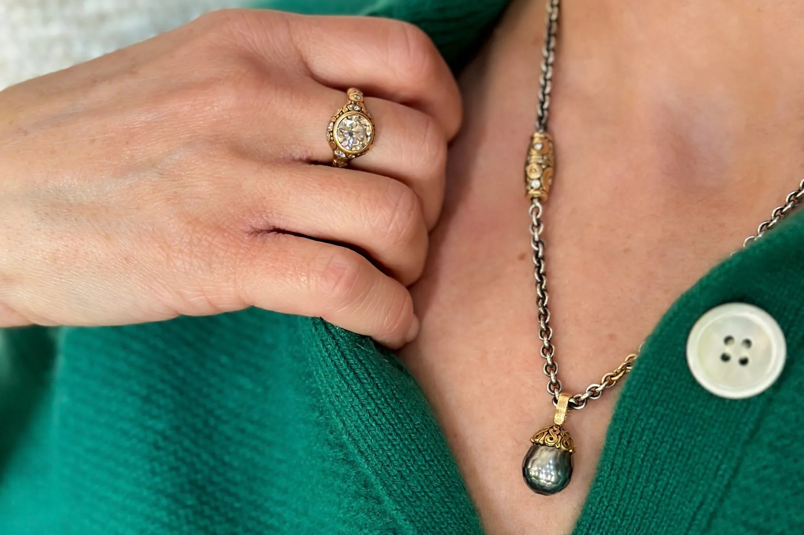 Close-up of a hand wearing a gold ring and a necklace with a pendant, against a green background.