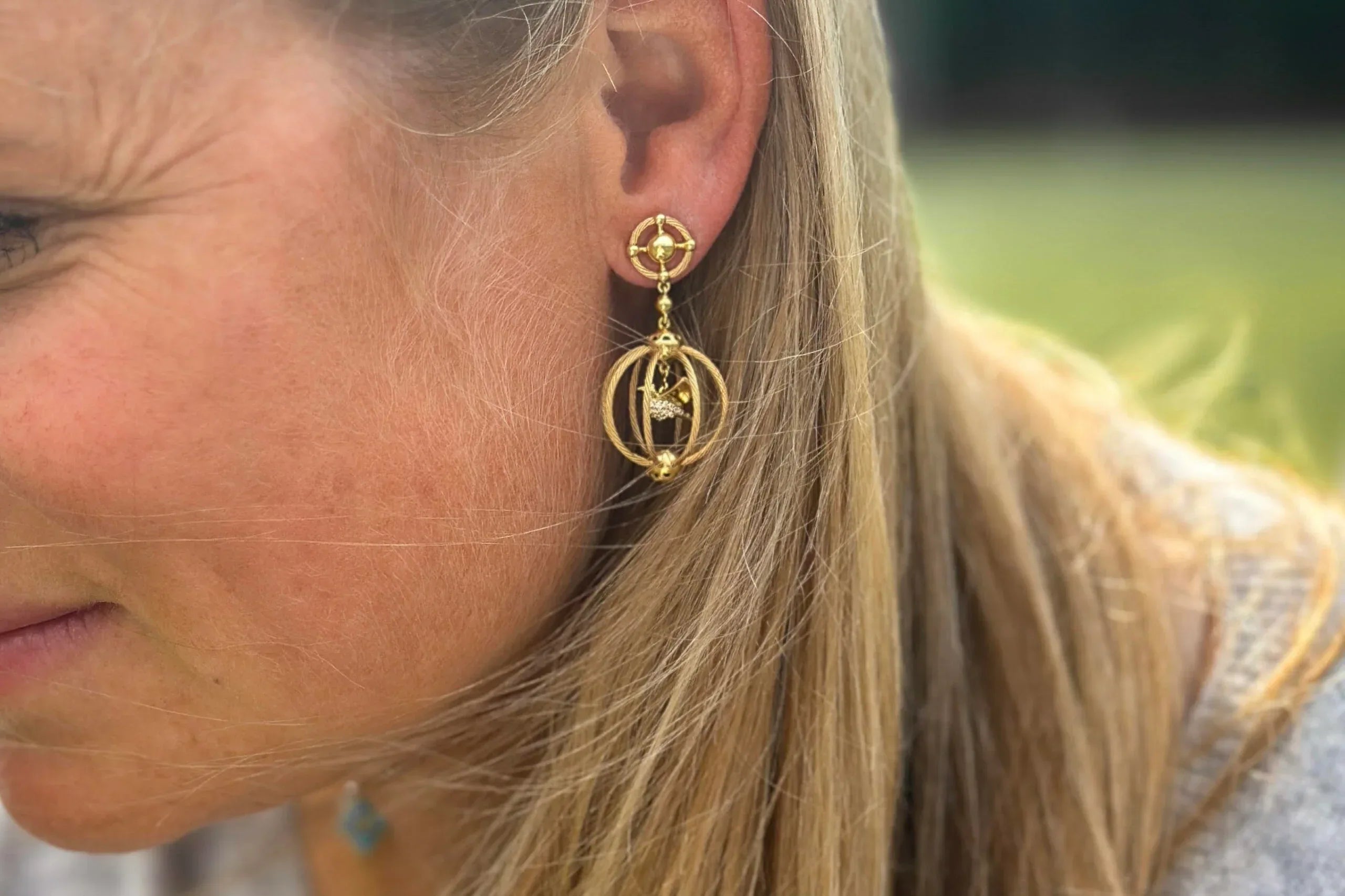 Close-up of a woman wearing gold earrings with a blurred outdoor background