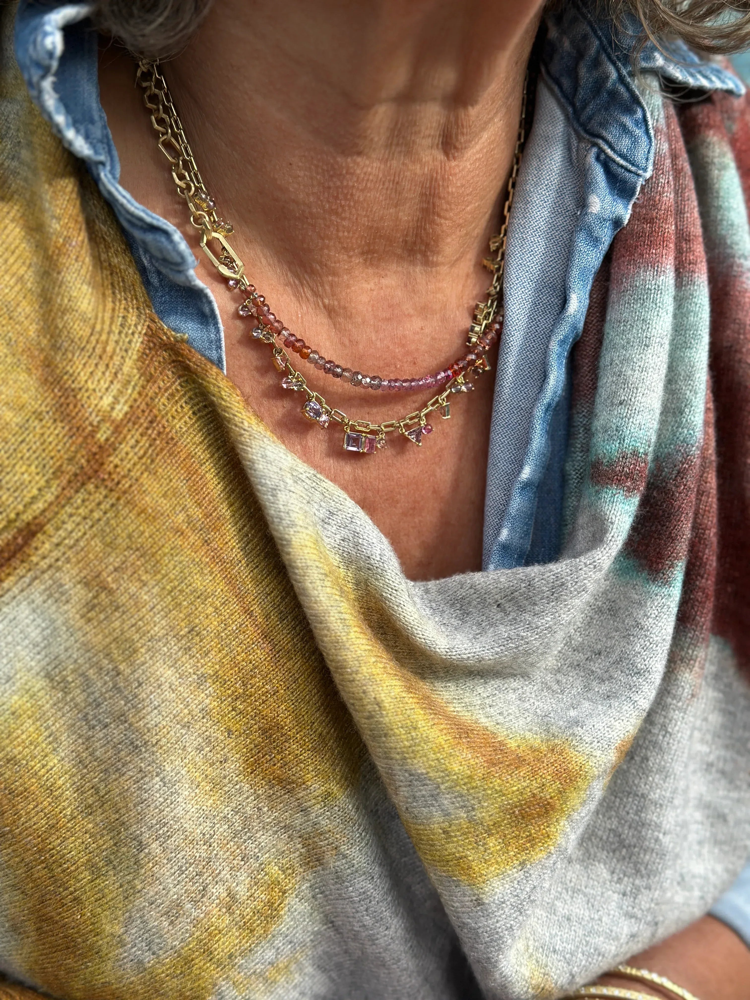 Close-up of a person wearing a gold necklace with a patterned scarf and shirt.