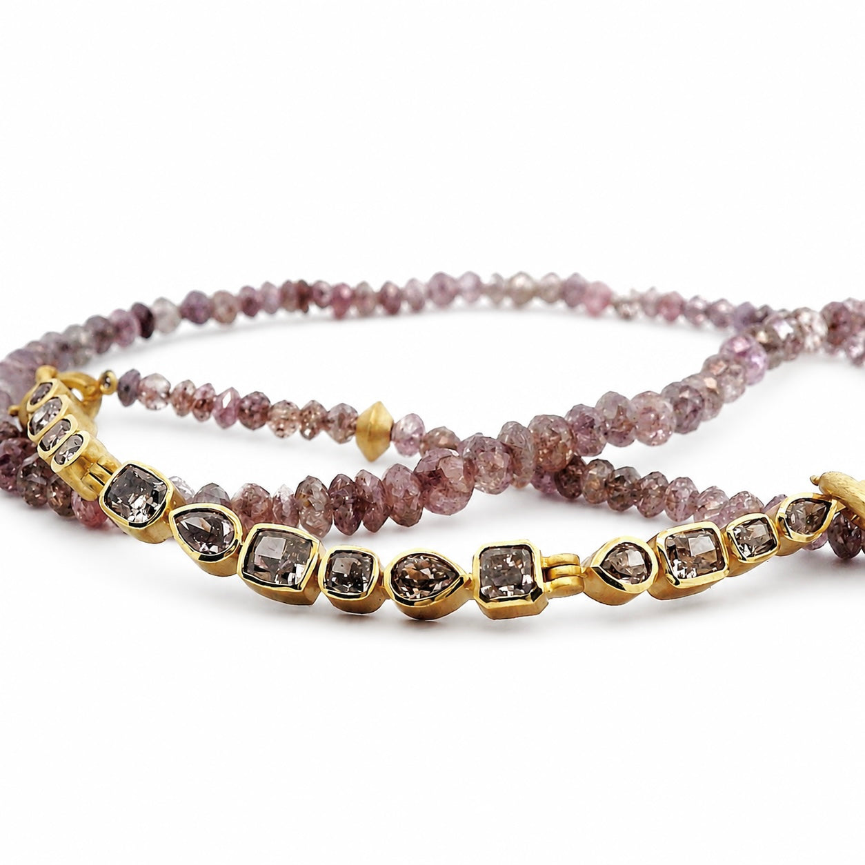 A gold-plated beaded bracelet featuring clear marquise and round gemstones with smoky brown centers, layered over a pinkish-purple beaded strand on a white background.