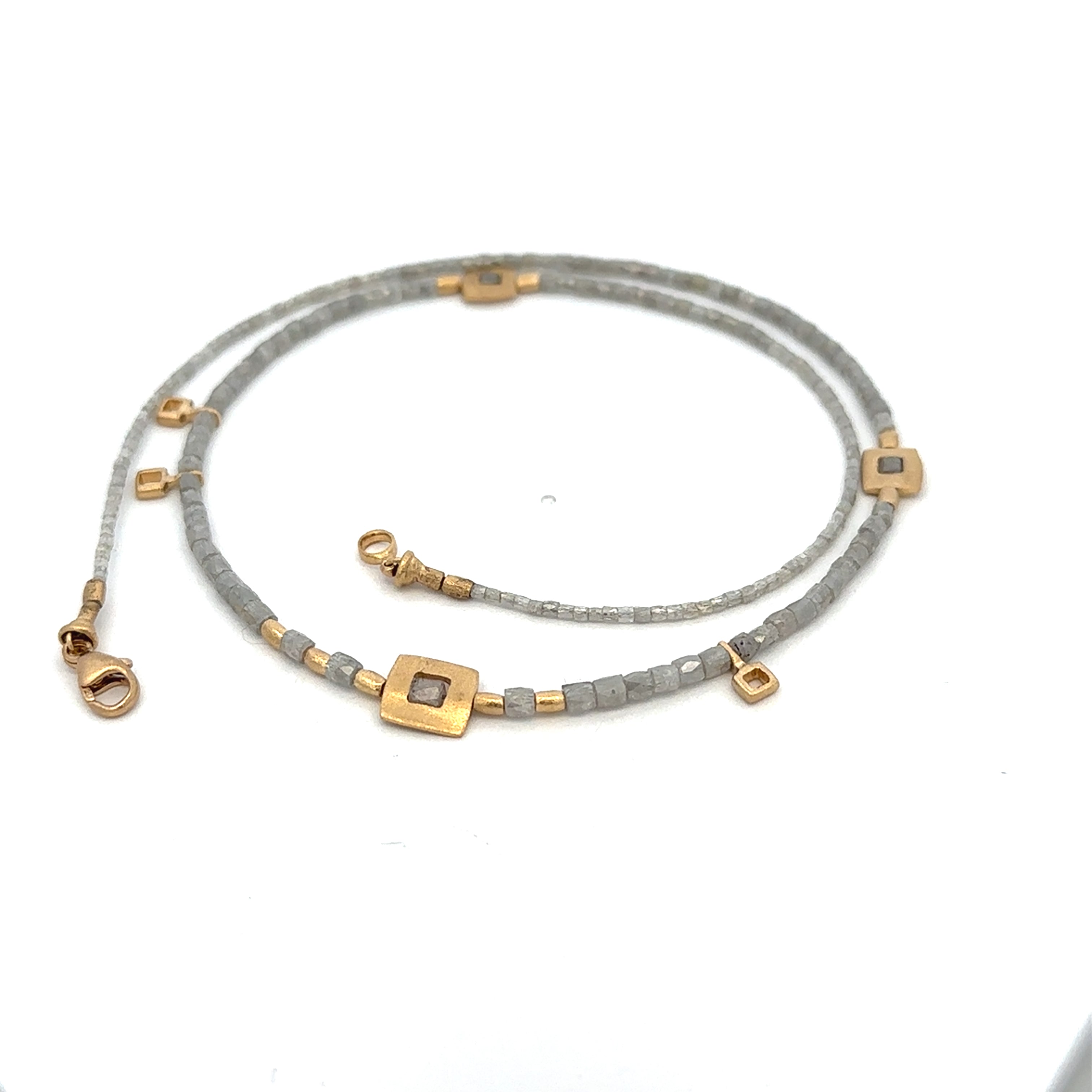 A delicate double-strand beaded necklace in gray and gold, featuring square gold charms with small gray inlays, displayed on a clean white background.