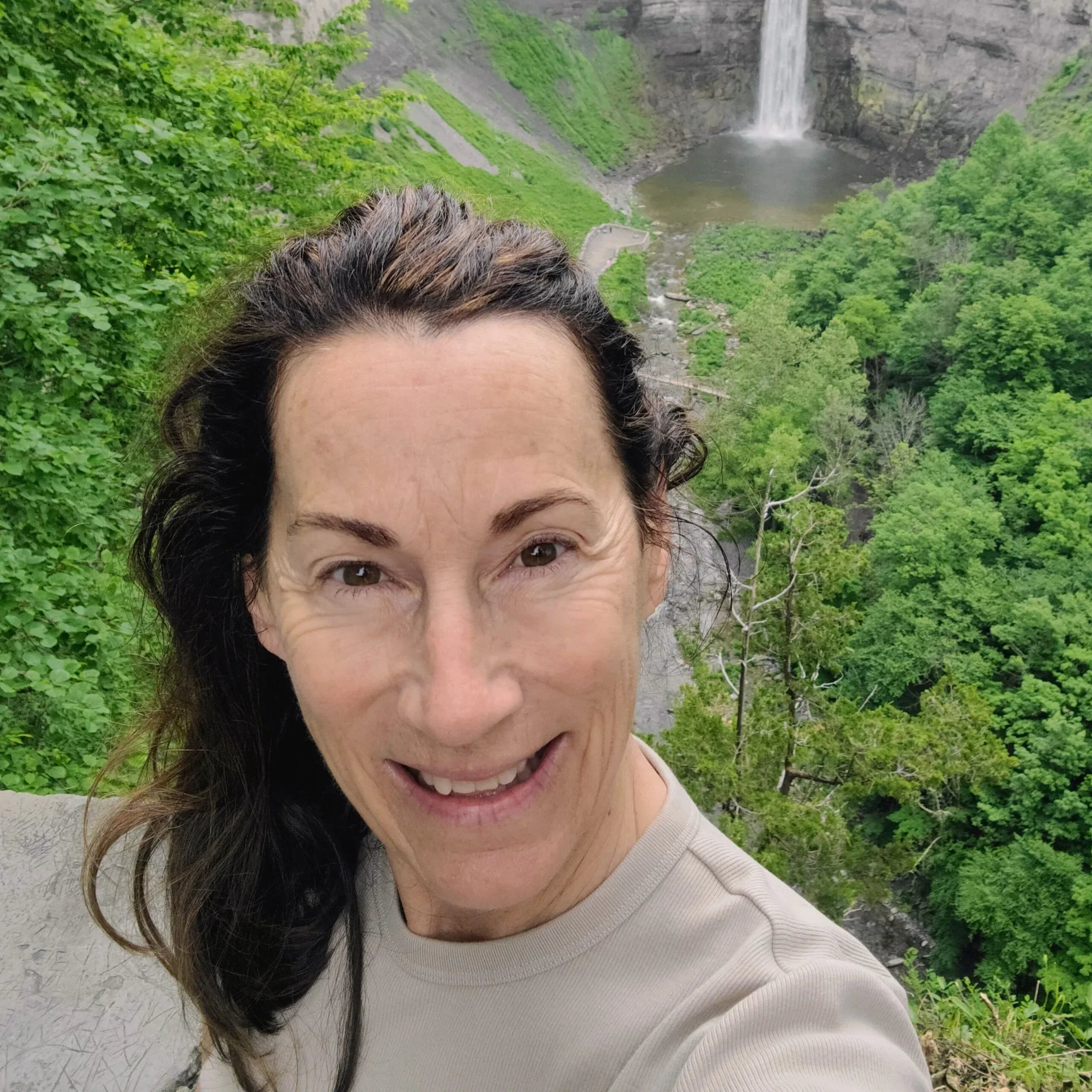 Woman taking a selfie with a scenic waterfall and lush greenery in the background.  Carol Huber - Stratton Store Sales