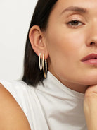 A woman in a sleeveless white top rests her chin on her hand, showcasing Yellow Gold and Diamond Hinged Hoop Earrings. Only the lower half of her face and ear are visible, drawing attention to the sparkling stones.