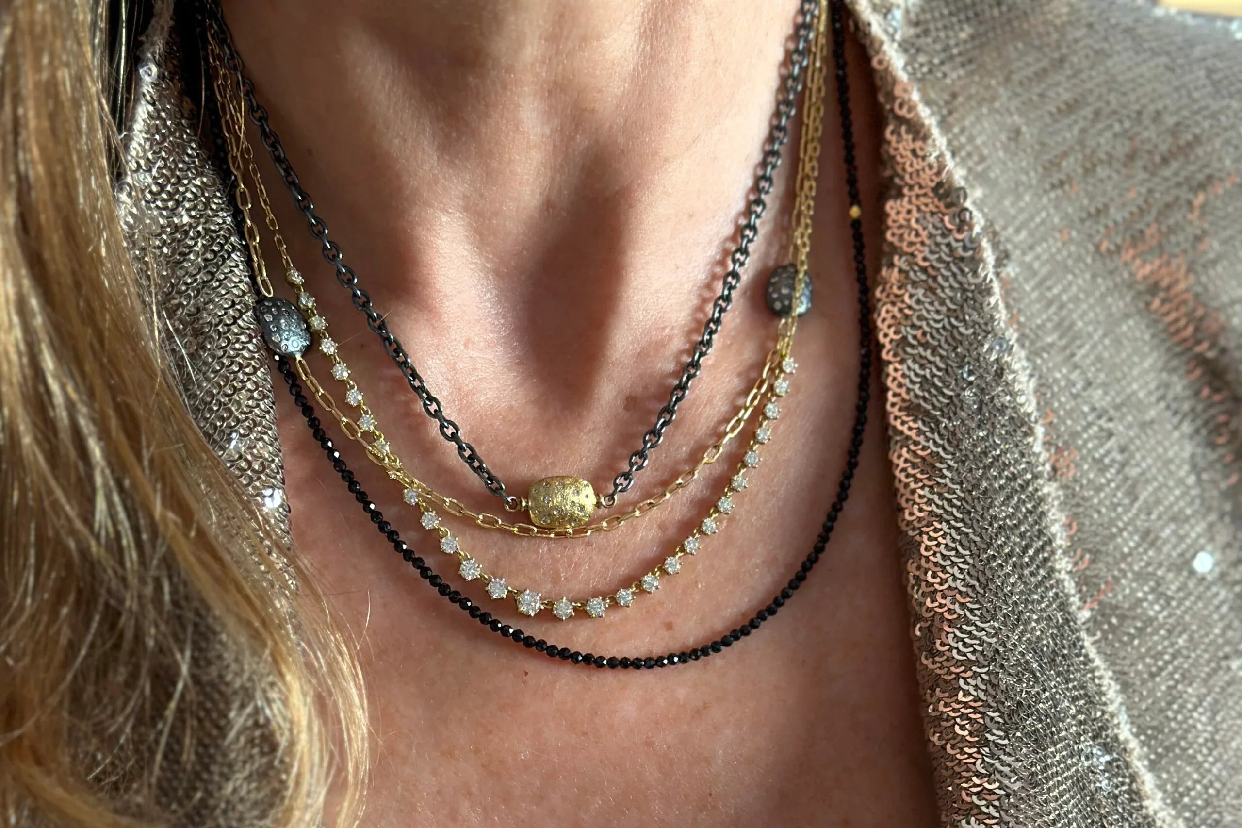 Close-up of a person wearing multiple necklaces with a textured garment.