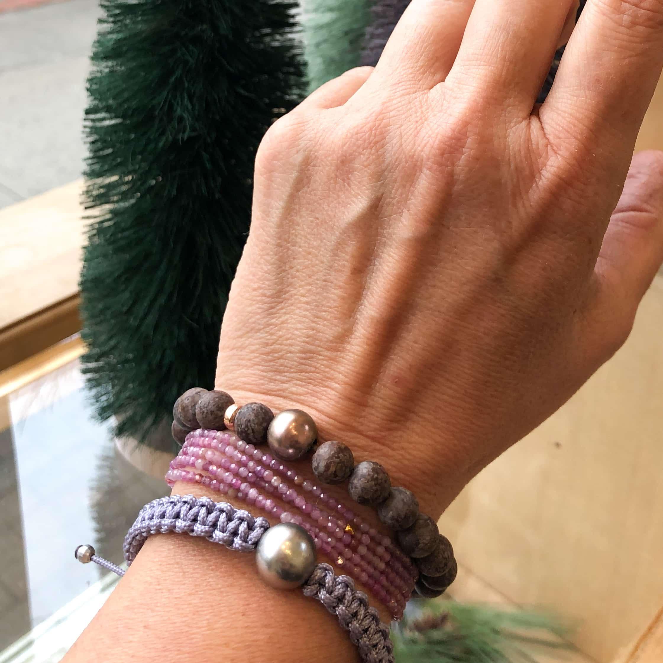 Person wearing a Tahitian Pearl and Snowflake Obsidian Bracelet on their wrist in front of a window and small fake plastic tree