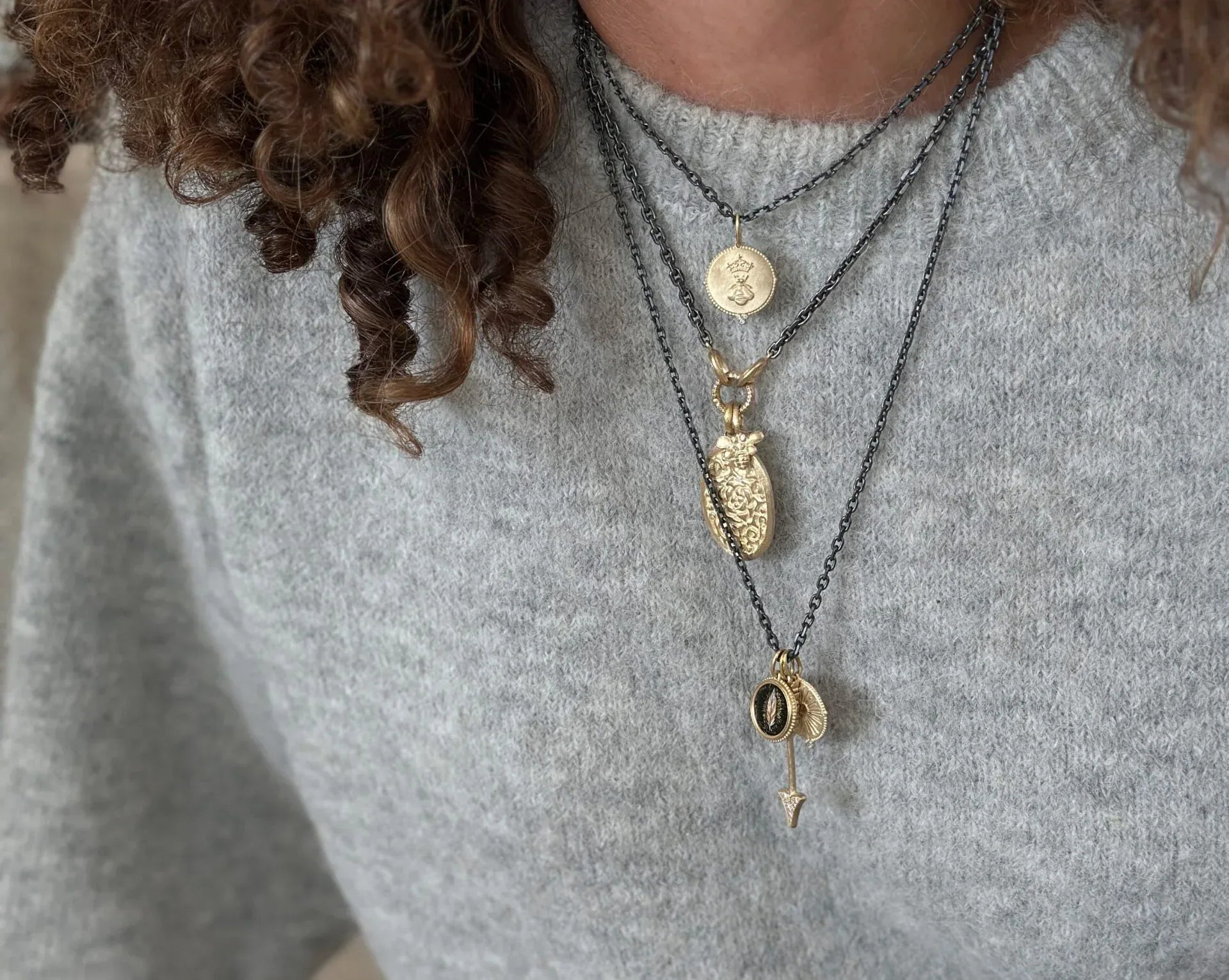 Person wearing multiple necklaces with various pendants on a gray sweater.