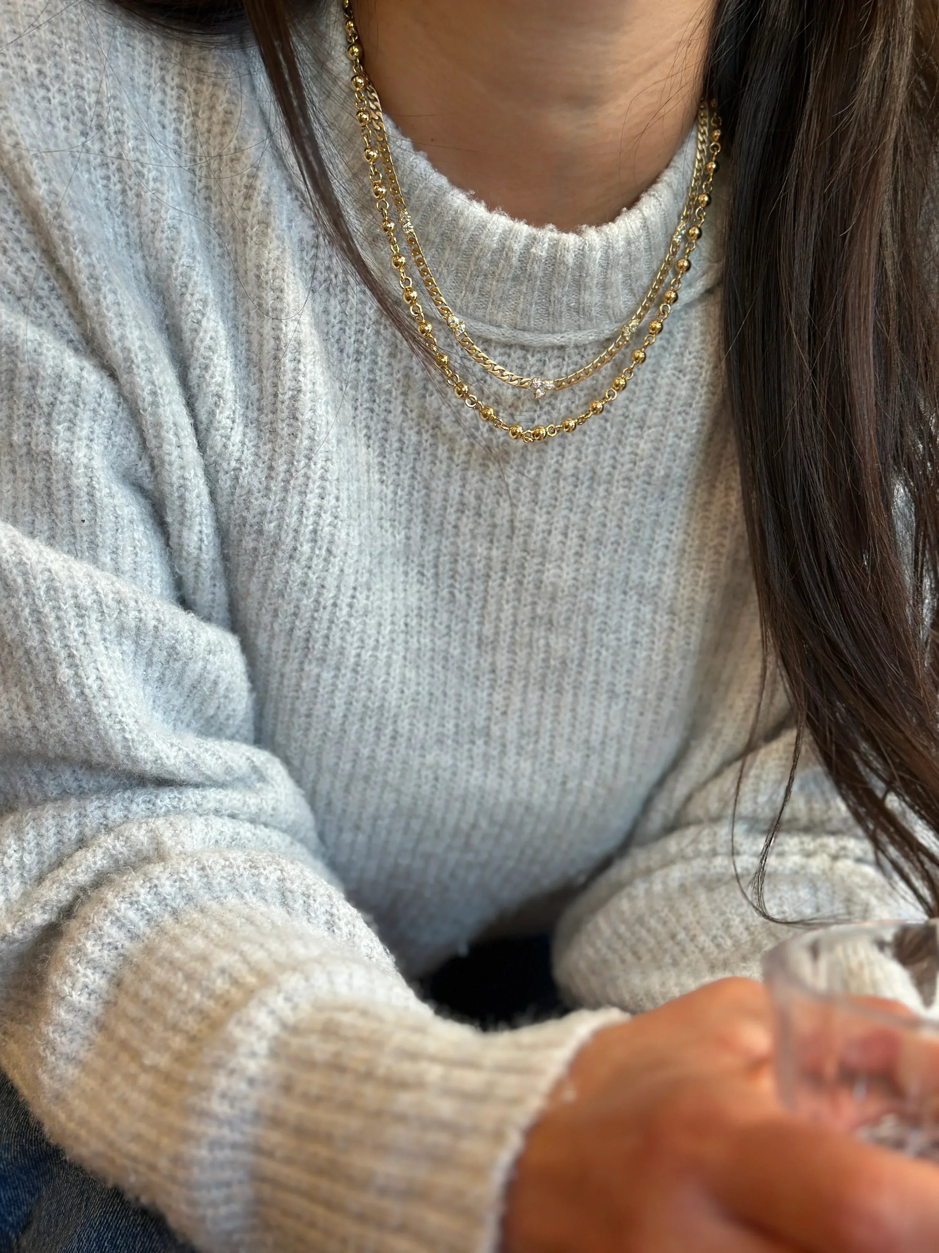 Person wearing a light gray sweater with gold chain necklaces, holding a small object.