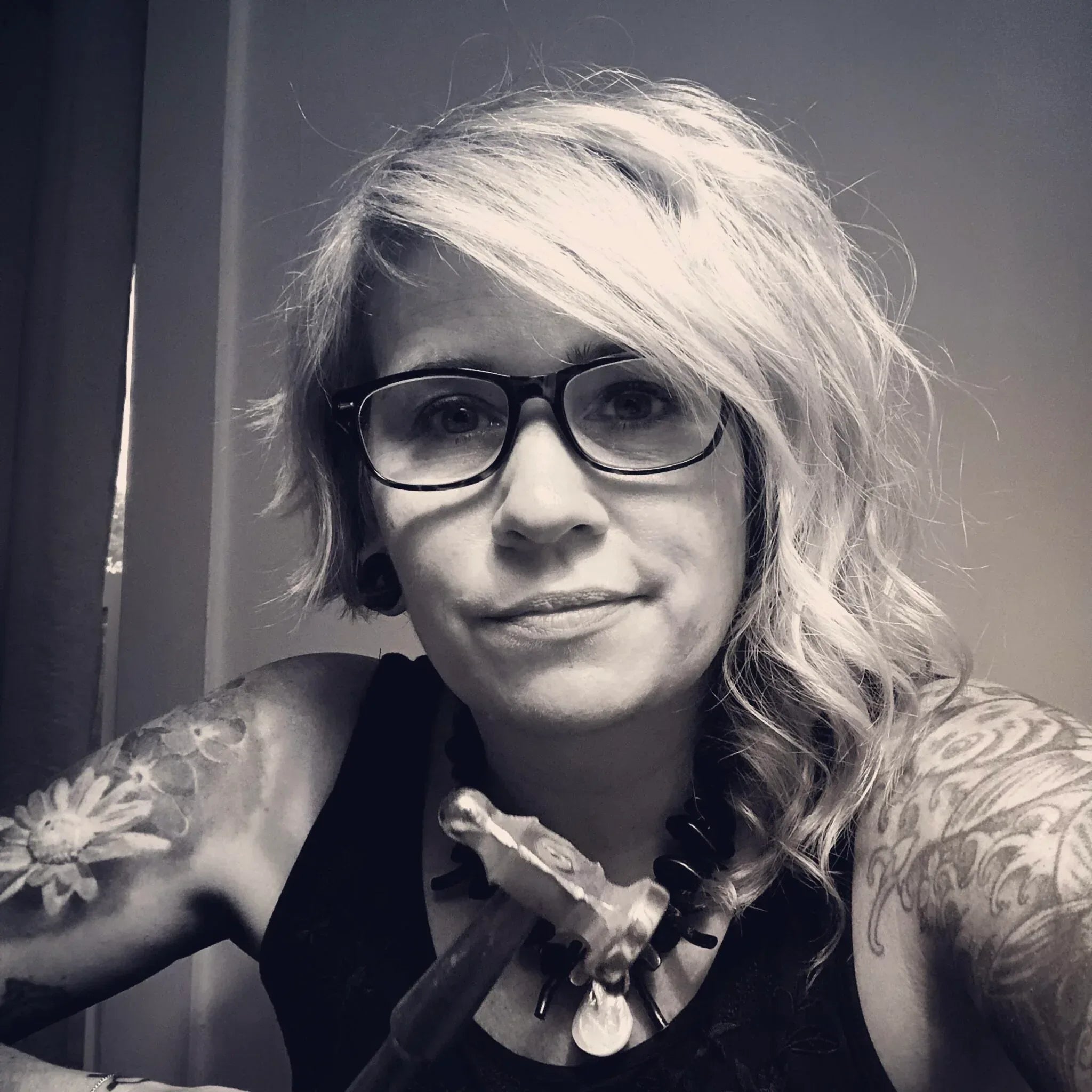 Black and white portrait of a woman with tattoos and glasses.