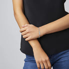 Person wearing a black top and blue jeans with gold bracelets on a gray background