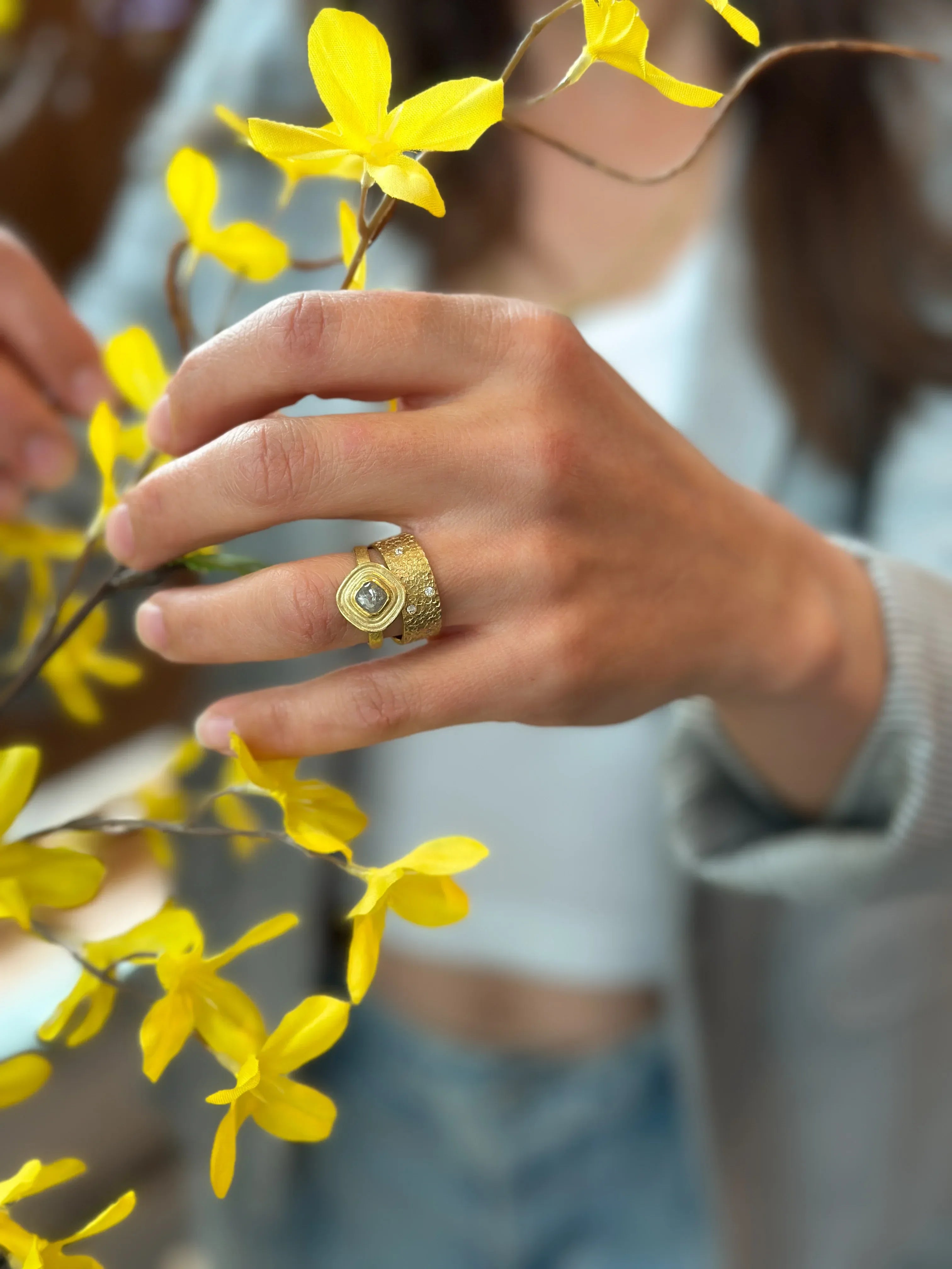 Person wearing a gold ring with a diamond, holding yellow flowers.