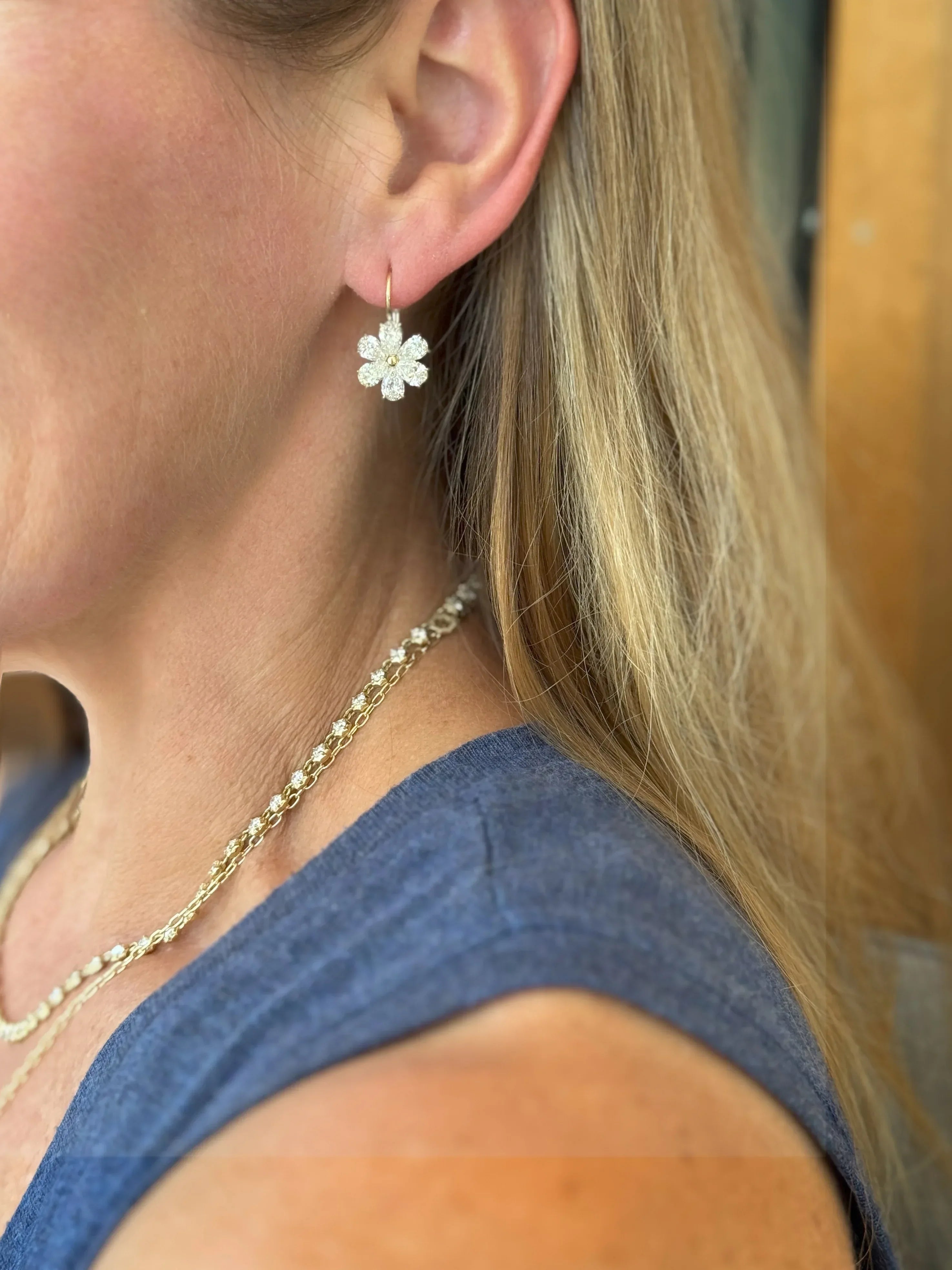 Close-up of a person wearing a floral earring and gold necklace.
