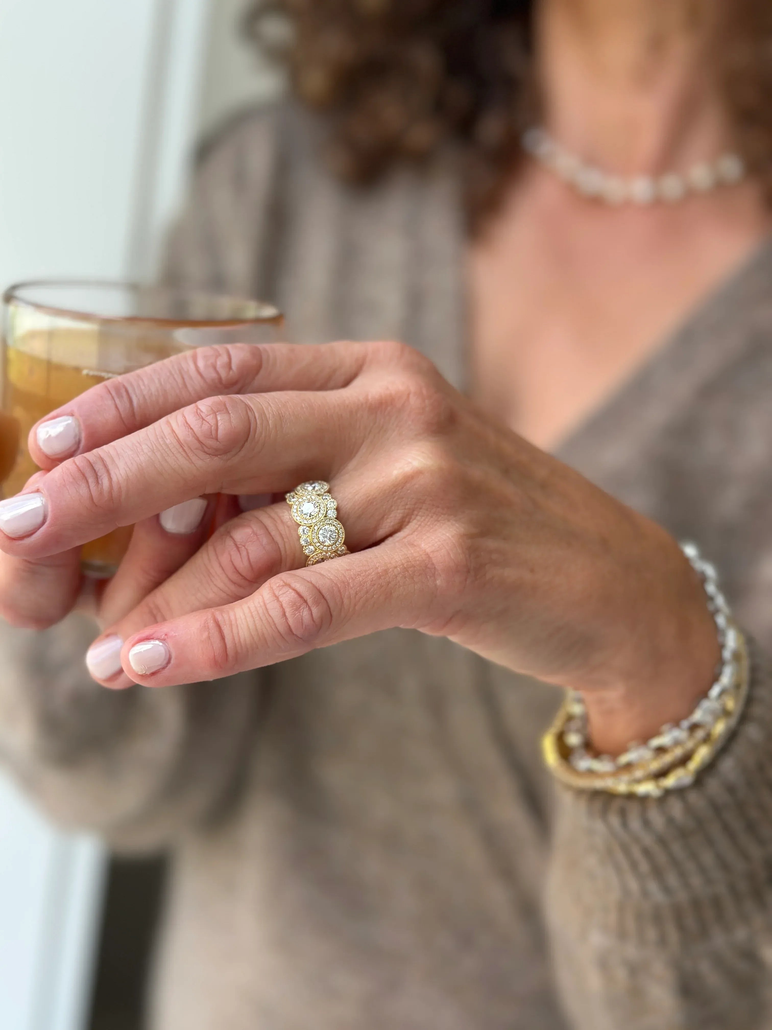 Person holding a glass of iced coffee with a focus on their hand wearing a diamond ring.