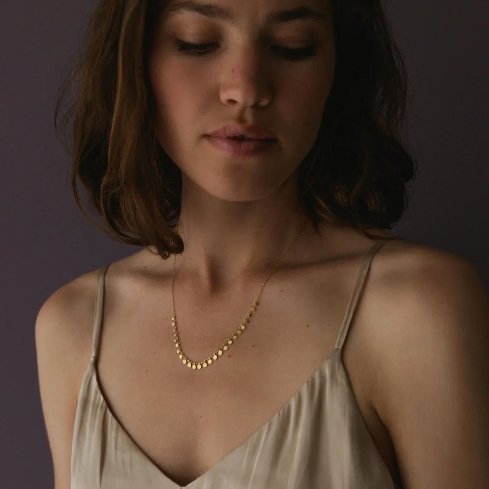 Woman wearing a gold necklace against a dark background