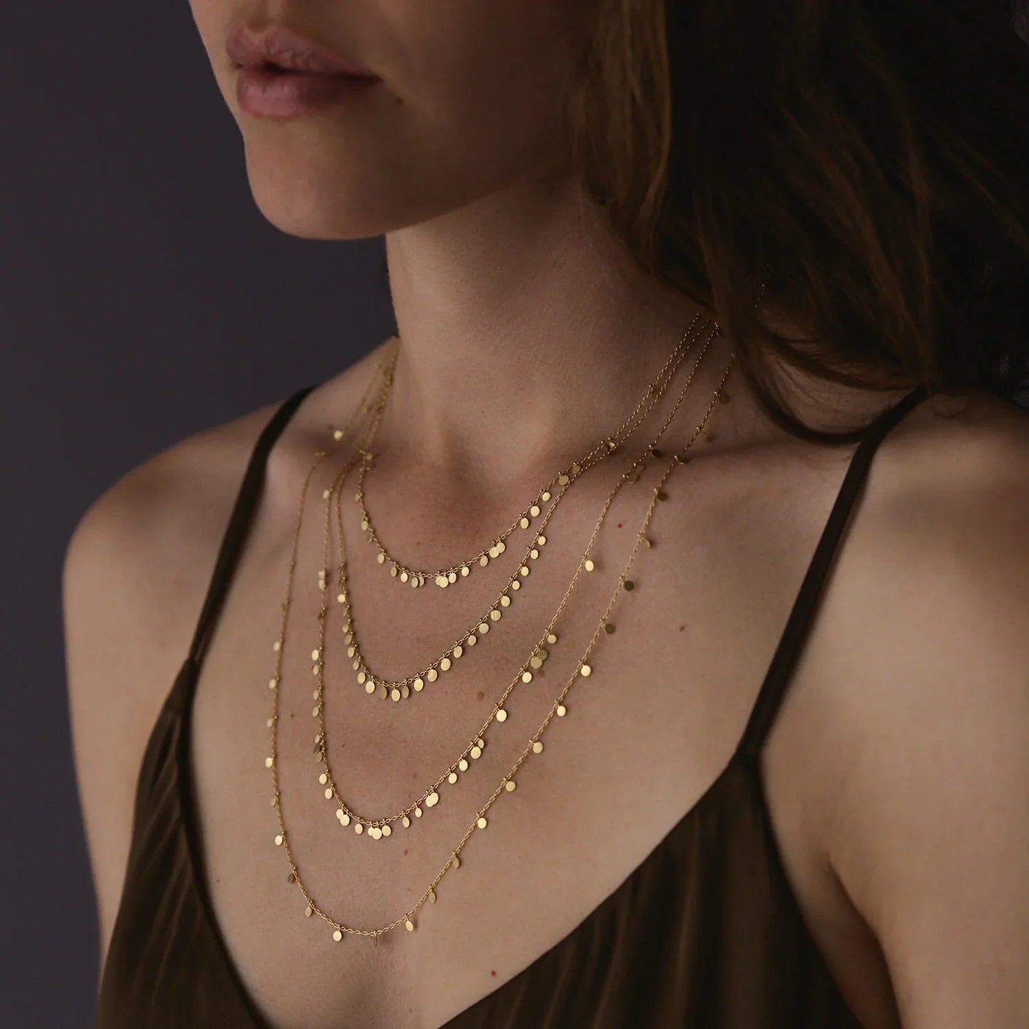 Close-up of a woman wearing multiple gold necklaces against a dark background