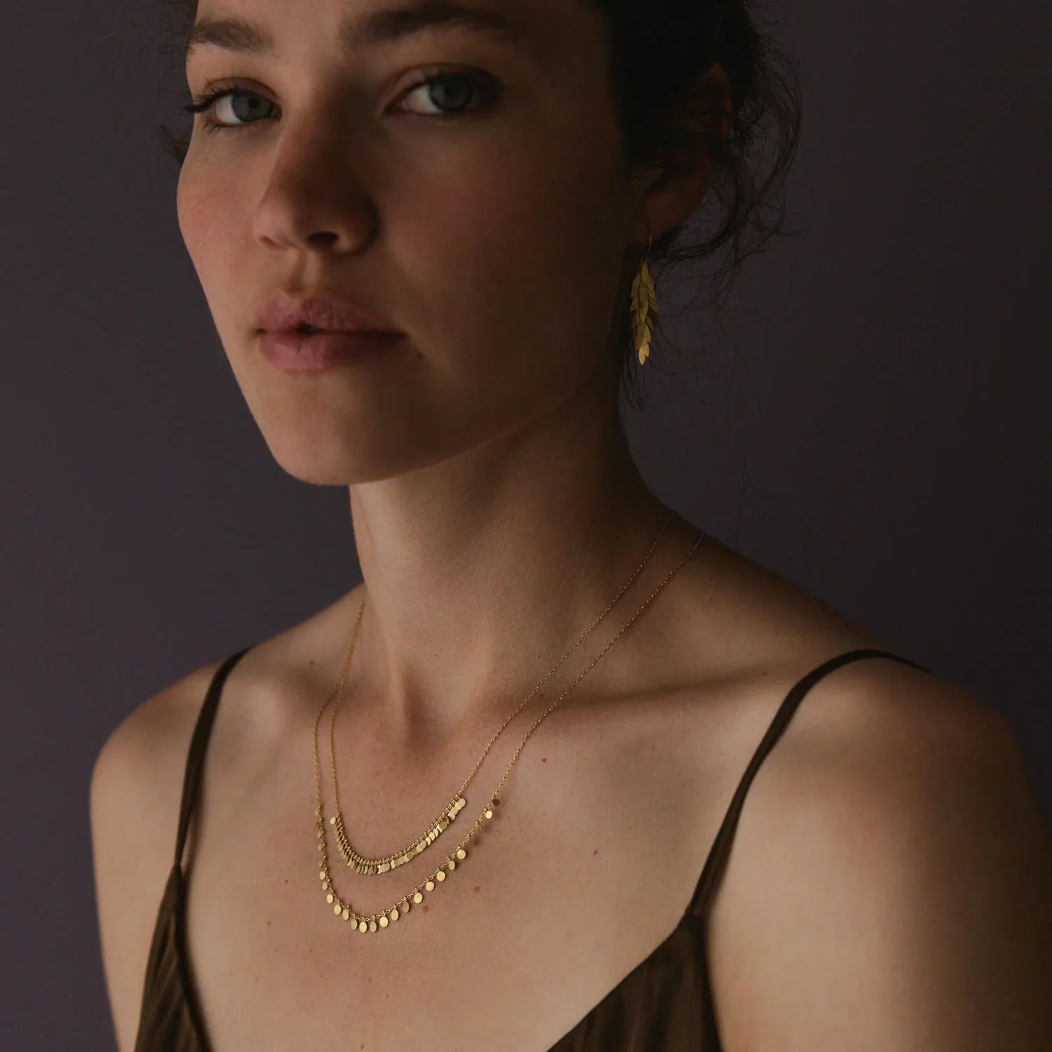 Woman wearing a gold necklace and earring against a dark background
