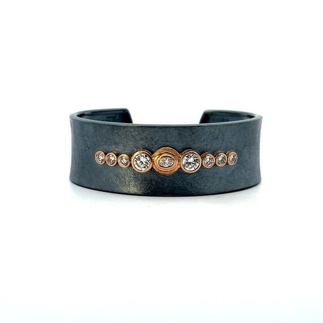 A wide black cuff bracelet with a row of small gold and clear gemstone accents across the front, photographed on a clean white background.