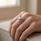 Platinum Diamond Ring design By Adel Chefridi on a womens hand with soft light and fabricate under the hand that is part of a couch