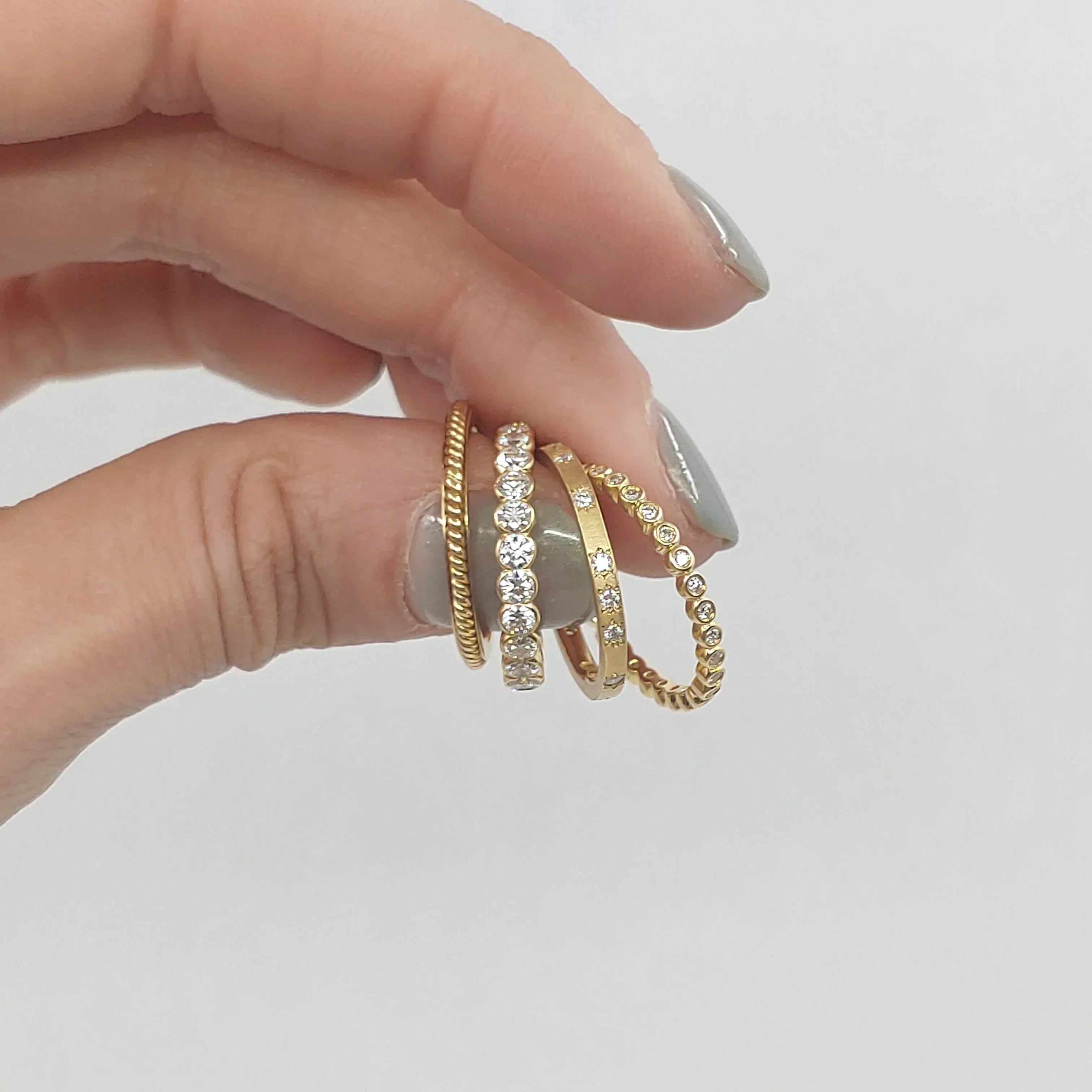 Hand wearing three gold rings with different designs on a light gray background