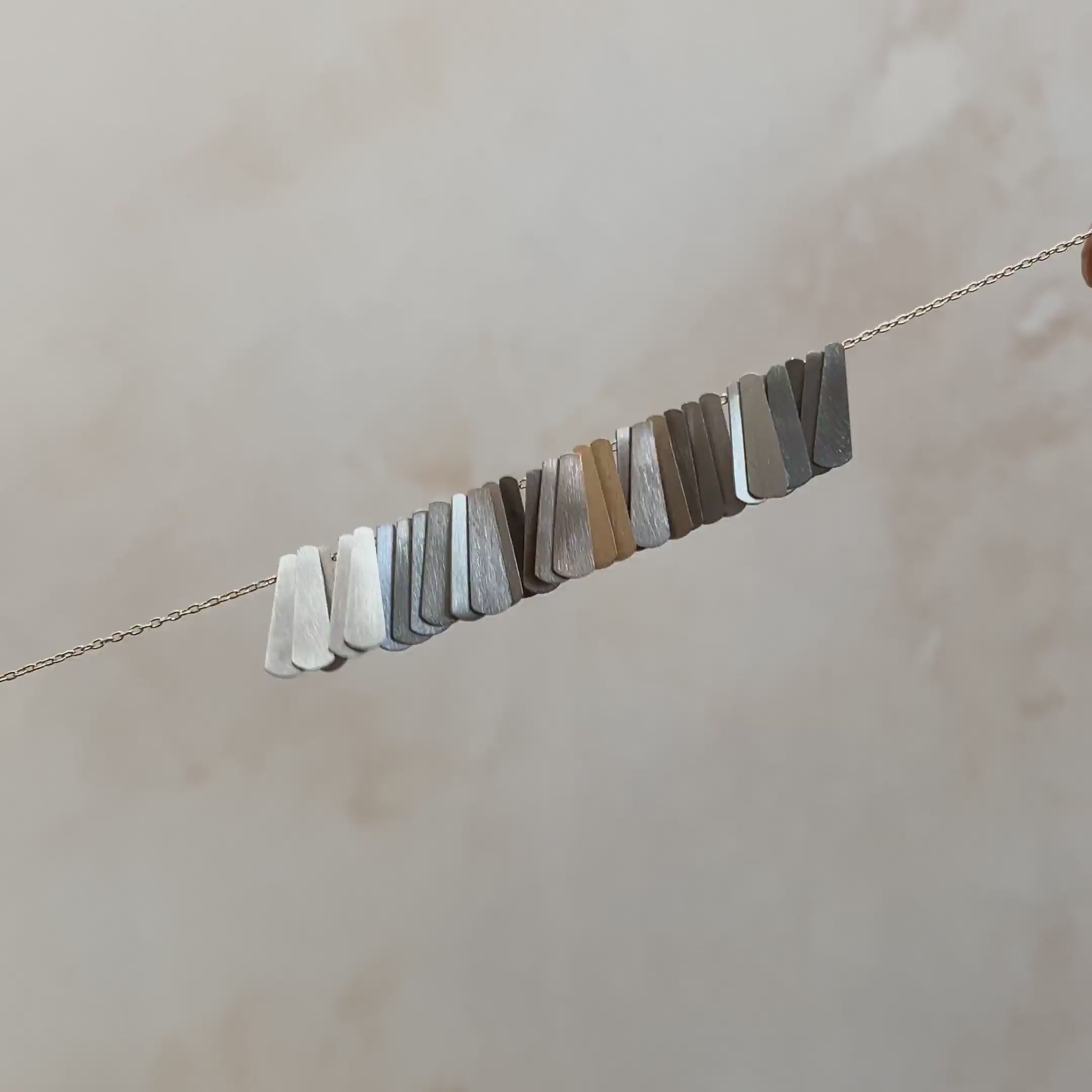 Video of a silver chain with different colored flat charms that shimmer in the light.