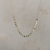 Video of a gold chain with gold dot pendants hanging from the chain and shimmering in the light on a grey background.